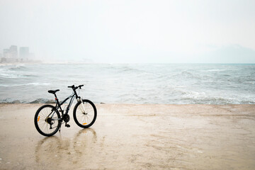 Obraz premium Alone Black Bicycle on the beach on rainy day with waves