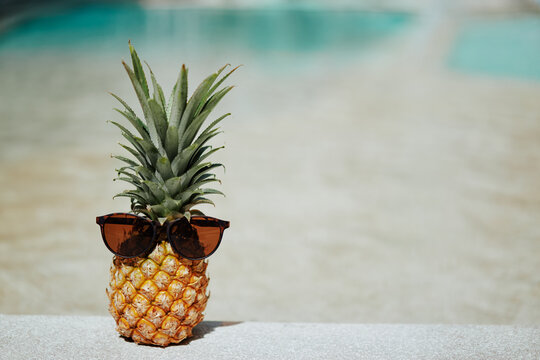 Tropical vacation concept. Pineapple with sunglasses near a swimming pool.
