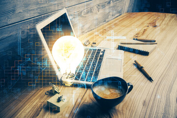 Computer on desktop in office with bulb icon hologram. Double exposure. Concept of idea.