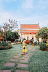 Travel by Asia. Young woman in hat and yellow dress walking near the Chalong buddhist temple on Phuket Island in Thailand.