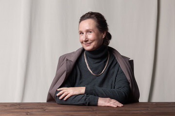 Fototapeta premium Good-looking and stylish caucasian elderly businesswoman sitting at the table and smiling. 