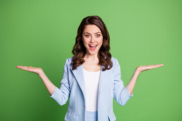 Photo of excited woman two arms palms hold empty space wear blue blazer isolated green color...