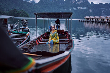 Obraz premium Travel by Thailand. Young woman in raincoat on traditional longtail boat sailing Khao Sok National Park Cheow Lan lake.