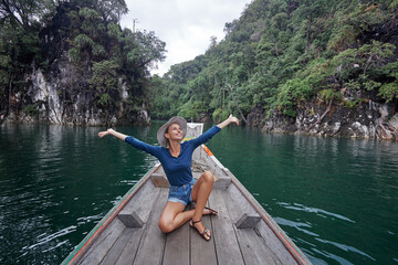 Happy vacation in Thailand. Pretty young woman taking sailing Khao Sok National Park lake on traditional longtail boat.