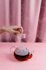 Female hand holding tea pot lid above kettle with the steaming fruit and berry tea,