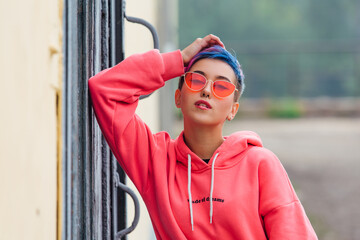 Portrait of a young girl with short colorful hair and nose piercing satanding near the wall with...