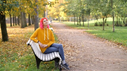 Walk in the autumn park. Young attractive woman with bright pink hair is resting in the park. Adult...