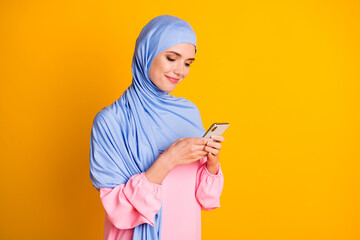 Profile side portrait of pretty focused cheery muslimah wearing hijab dress using gadget comment...