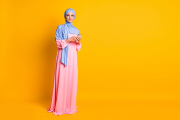 Fototapeta na wymiar Full length body size view of nice pretty elegant muslimah wearing hijab dress using device blog isolated on bright yellow color background