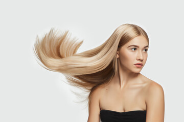 Tender. Beautiful model with long smooth, flying blonde hair on white studio background. Young caucasian model with well-kept skin and hair blowing on air. Concept of salon care, beauty, fashion.