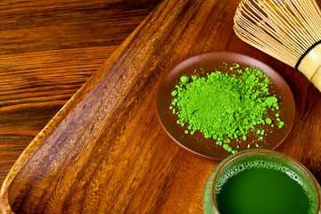 Green matcha tea in a cup with powdered matcha tea in a plate and bamboo matcha tea whisk also know as chasen on a wooden background. 