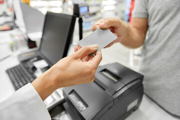 medicine, payment and finance people concept - close up of hand giving bank card to pharmacist