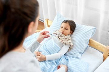 family, health and people concept - mother with thermometer measuring temperature of sick daughter lying in bed at home