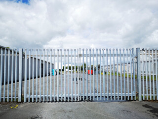 Security fence and gates outside a factory unit car park. The gates are closed and the factory is shut for the night.
