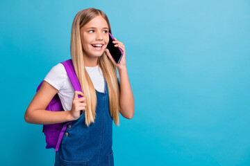 Photo of cool pretty teen girl looking empty space talk telephone wear bag denim dress isolated on pastel blue color background