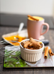 Heap of Turmeric roots in white bowl on table and unfocused turmeric powder, curcuma latte at background