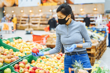 Young woman in protective mask and gloves choosing fruits in a supermarket or market.