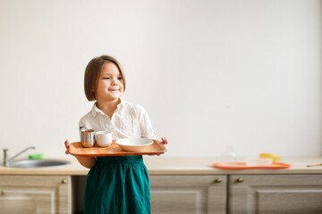 child girl in a linen apron with a tray lays the table, developing sensory activities in montessori...