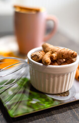 Heap of Turmeric roots in white bowl on table and unfocused turmeric powder, curcuma latte at background