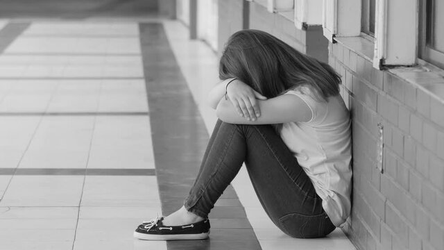 Young asian teenager upset seated on the school hallway pavement. Bullying concept. Slow motion