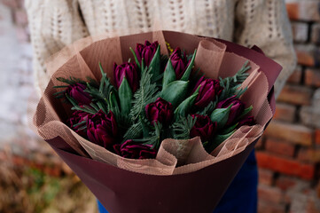 Bouquet of flowers in burgundy package in hands.