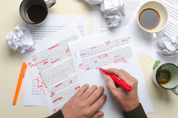 Top view of cups of coffee, crumpled paper, documents and red marks on it.Man proofreading story...