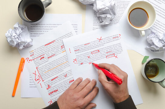 Top view of cups of coffee, crumpled paper, documents and red marks on it.Man proofreading story and has lot of work