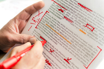 Man holding red marker and proofreading the story.Closeup of document and red marks on it