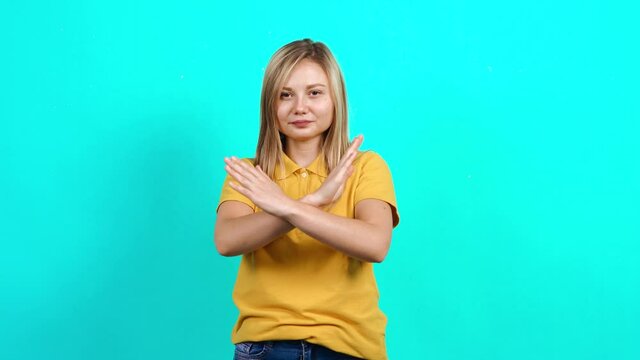 The modest young woman puts her palm in front of her and says stop. It shows the sign that so far. Beautiful Caucasian woman in yellow T-shirt and long blond hair standing on blue background. A little