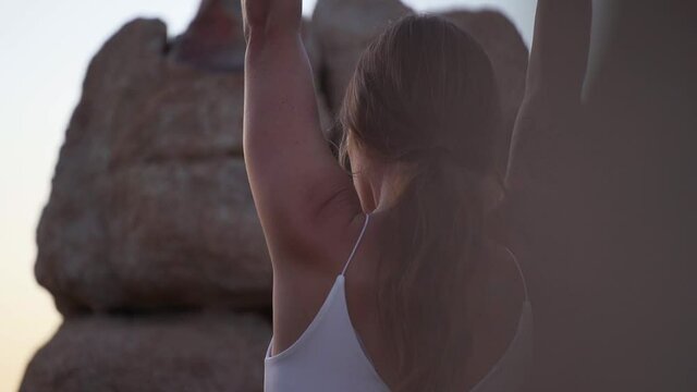 Girl with tattoo on her arm doing stretch on rock during sunset at Joshua Tree, California, slow motion