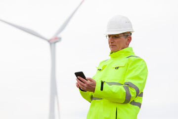 Mature engineer looking at smart phone in front of a wind turbine