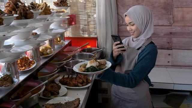 portrait of young muslim woman take photos of food she sale at warung nasi padang tradtional restaurant