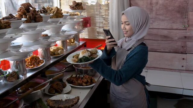 portrait of young muslim woman take photos of food she sale at warung nasi padang tradtional restaurant