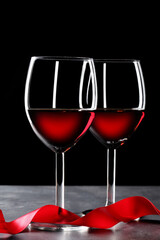 two red wineglass and a red ribbon on slate table and black background with copy space for your text