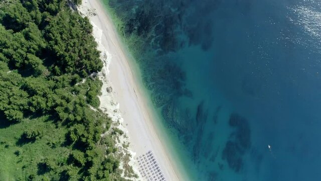 Aerial zenithal view of the San Michele beach near Sirolo, Conero mountain Marche (Italy) in the summer season.The sandy beach with umbrellas and sunbeds divides the steep cliff from the blue sea.