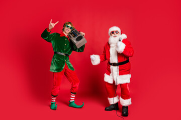 Photo of two crazy men elf hold boom box show horns santa sing mic wear sunglass x-mas costume coat hat isolated red color background