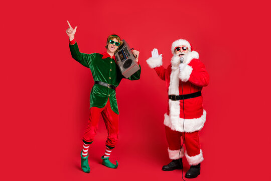 Photo of two carefree people elf hold vintage radio santa sing microphone wear sunglass x-mas costume coat cap isolated red color background
