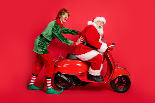 Full length photo of two people elf santa ride moped stuck wear x-mas costume coat cap boots isolated red color background