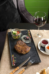 Grilled Ribeye Steak with vegetable salad on stone board and glass of red wine on the table at restaurant