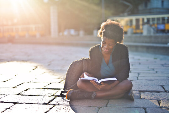 young woman reads a book in the street