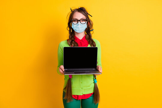 Portrait of attractive girl holding in hands demonstrating laptop screen wear mask isolated bright yellow color background