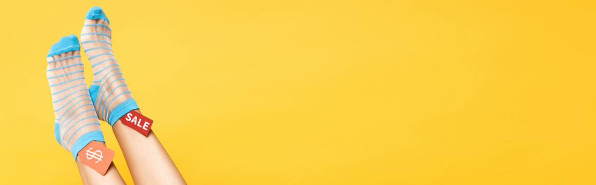 Female legs in socks and tags with dollar symbol and sale word isolated on yellow, banner