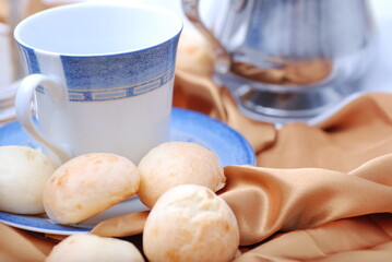 A cup of coffee or tea and silver platery on a luxurious table with cheese bread.