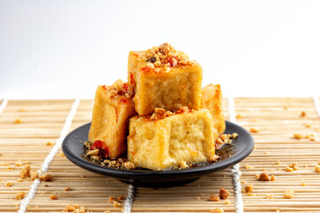 Fried tofu is stacked and sprinkled with peanuts and sweet sauce on black plate, food of vegetarian, popular food of vegetarian festival.