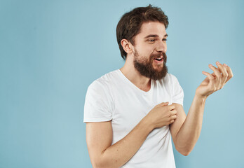 An energetic man gesturing with his hands on a blue background and a thick beard in a white t-shirt