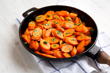 Homemade Sauteed Carrots in a cast iron pan on a white wooden surface, side view. Close-up.