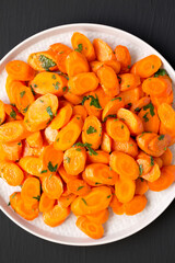 Homemade Sauteed Carrots on a plate on a black surface, top view. Flat lay, overhead, from above. Close-up.