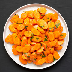 Homemade Sauteed Carrots on a plate on a black surface, top view. Flat lay, overhead, from above.