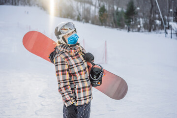Woman snowboarder on a sunny winter day at a ski resort wearing a medical mask during COVID-19...
