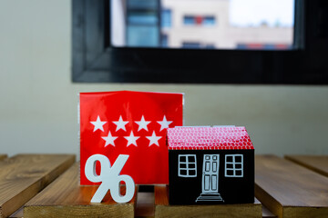 Front view of a miniature house, next to the flag of the Autonomous Community of Madrid, in Spain, and a percentage symbol.  To represent concepts of crisis, real estate, property or various problems.